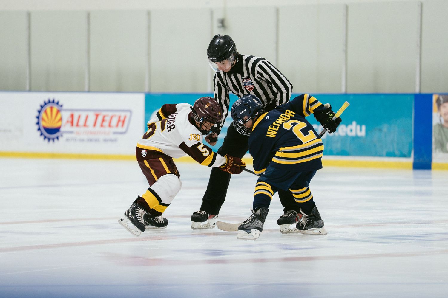 Two youth hockey players face off at center ice with a referee during a youth hockey game.