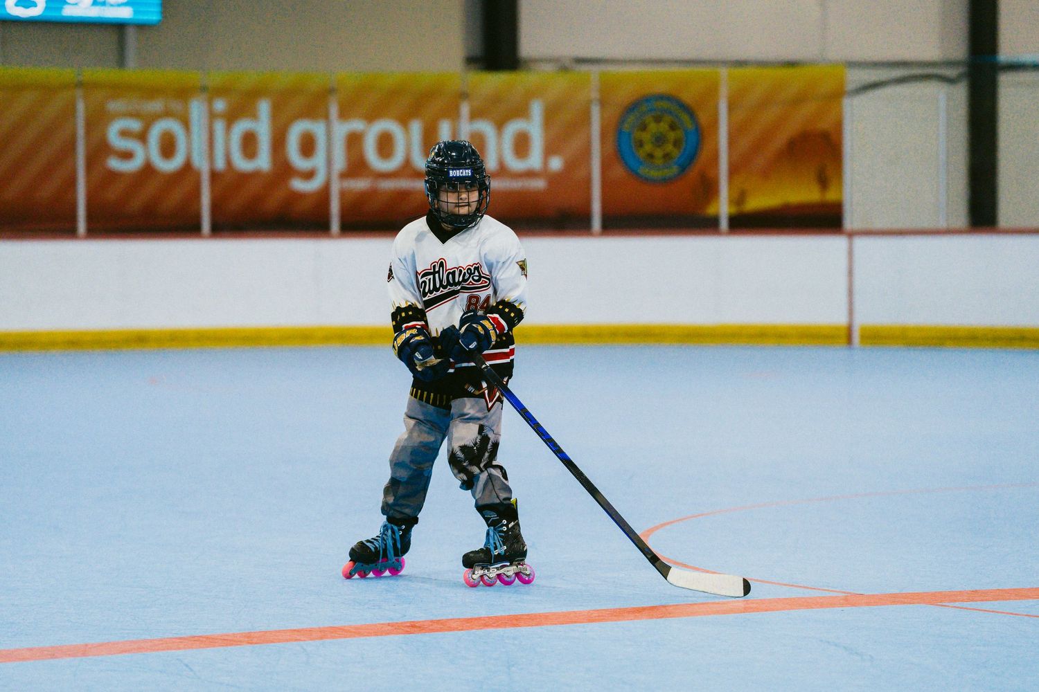 Young roller hockey player in full gear practices stick handling on a bright blue indoor rink.