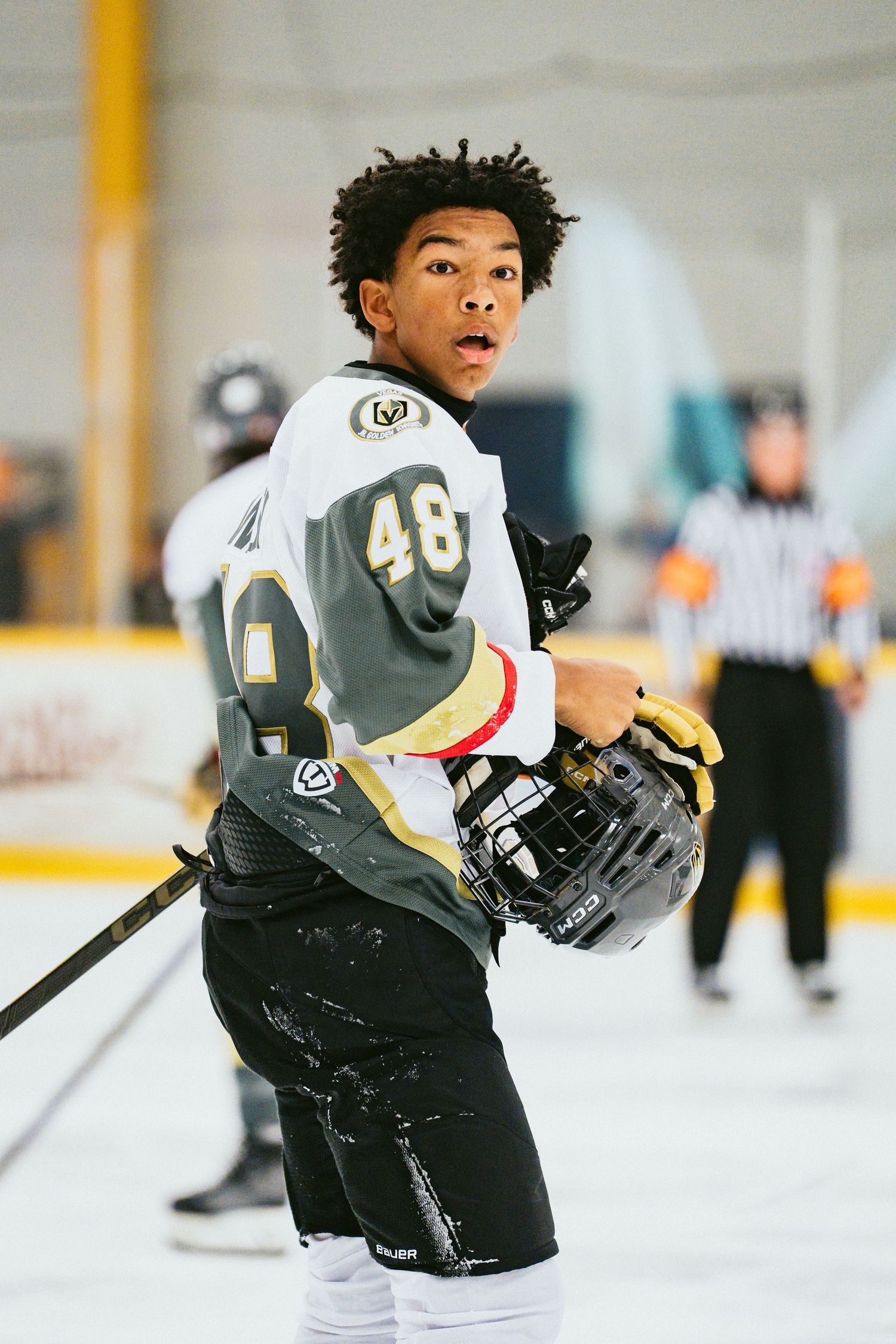 Young hockey player wearing number 48 in a Vegas Golden Knights style jersey stands on the ice during an indoor game.