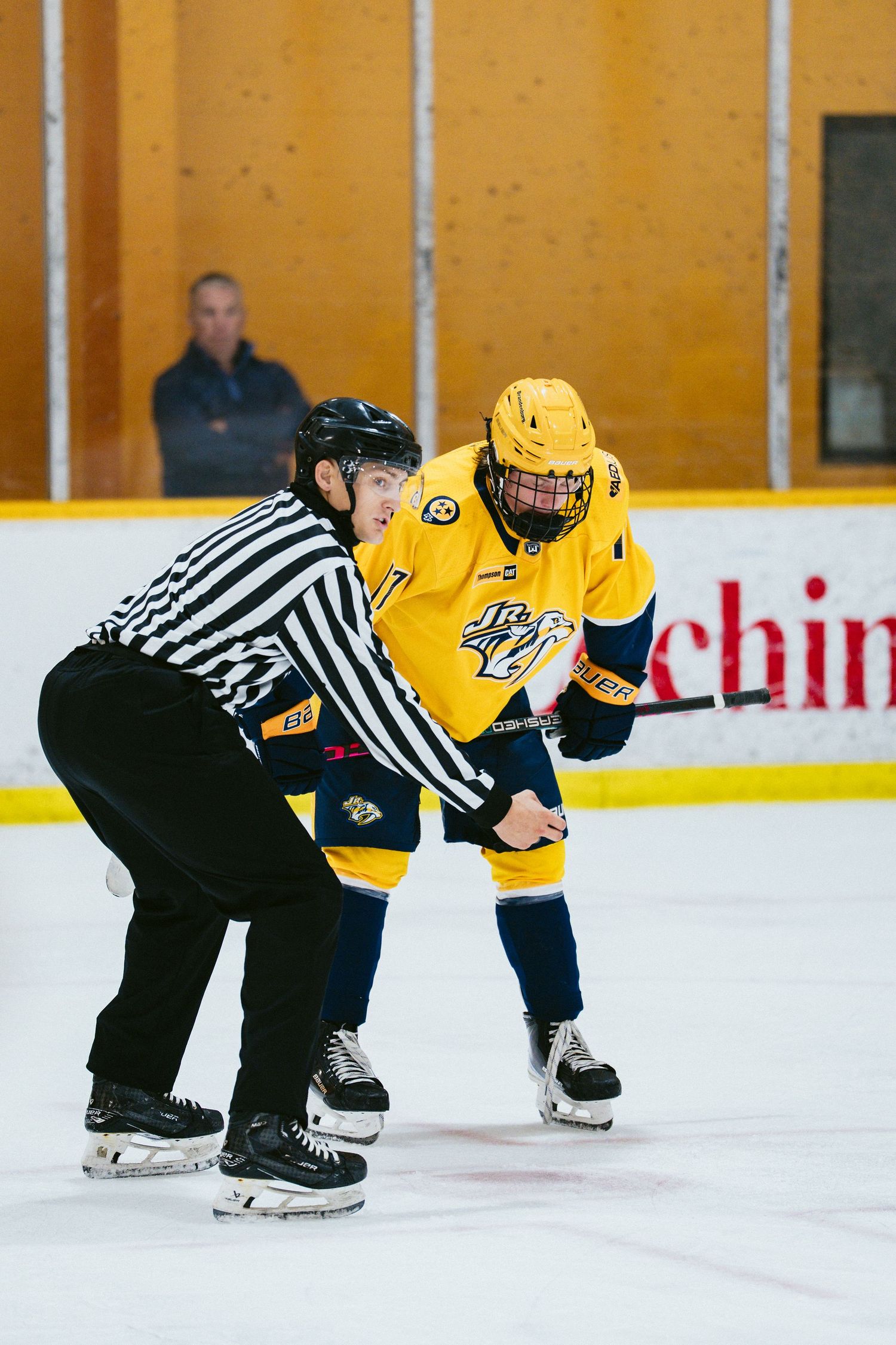 A hockey referee prepares for a face-off with a player in a yellow Nashville Predators jersey on the ice.