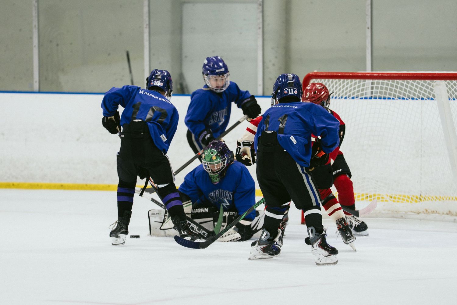Ice hockey players in blue uniforms compete near the goal during an indoor rink game.