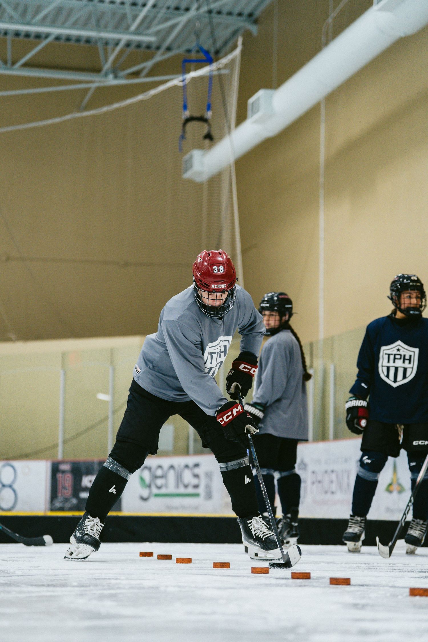 Hockey player in red helmet practices skating drills on ice during a TPH training session.