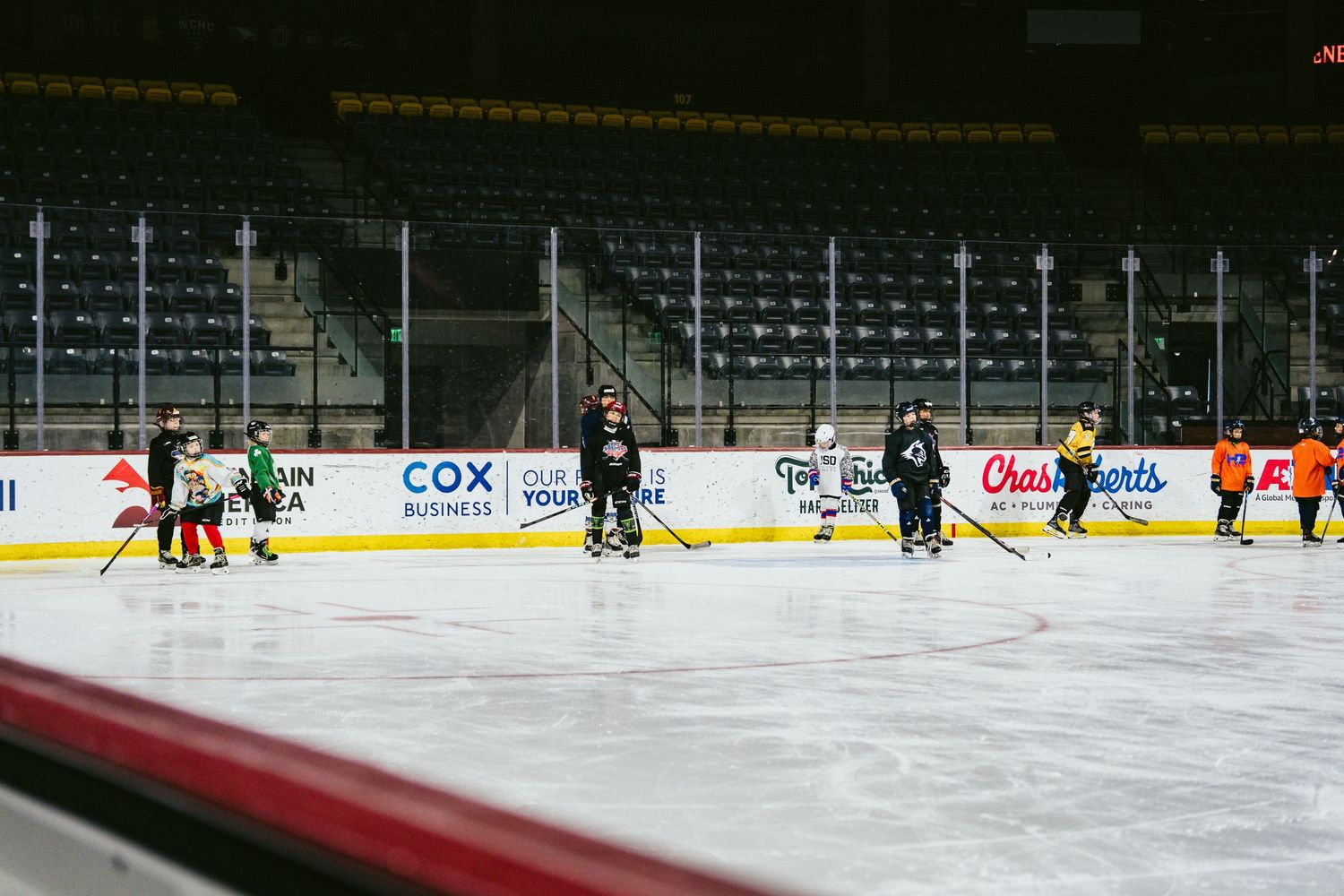 Youth hockey players practice on an indoor ice rink with Cox Business and arena sponsor signage visible.