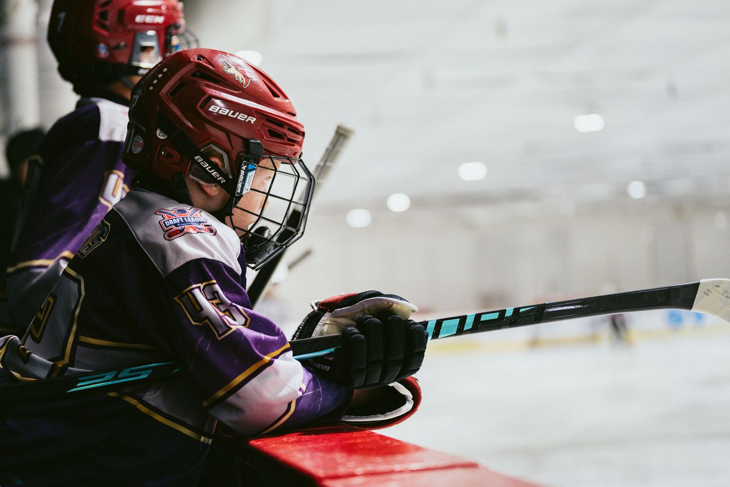 Young hockey player in red Bauer helmet resting on the boards during a youth ice hockey game.