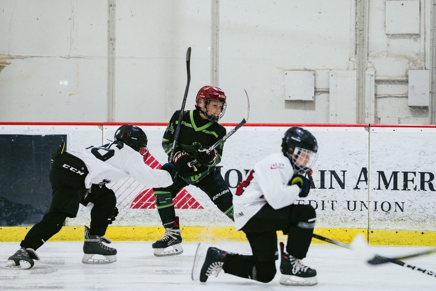 Young hockey player in green jersey skates between two opponents during a youth ice hockey game.