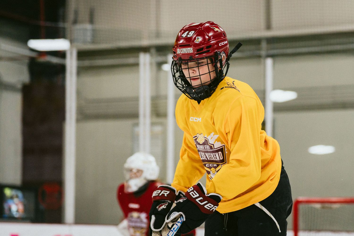 Young hockey player in yellow jersey smiling during youth ice hockey practice session.