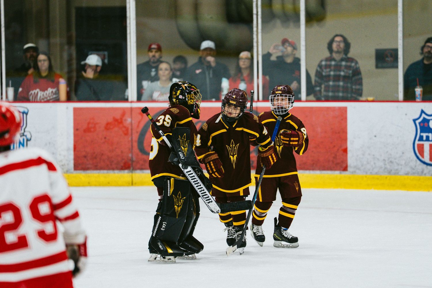 Indoor hockey game showing players from opposing teams spread across the rink with spectators watching.