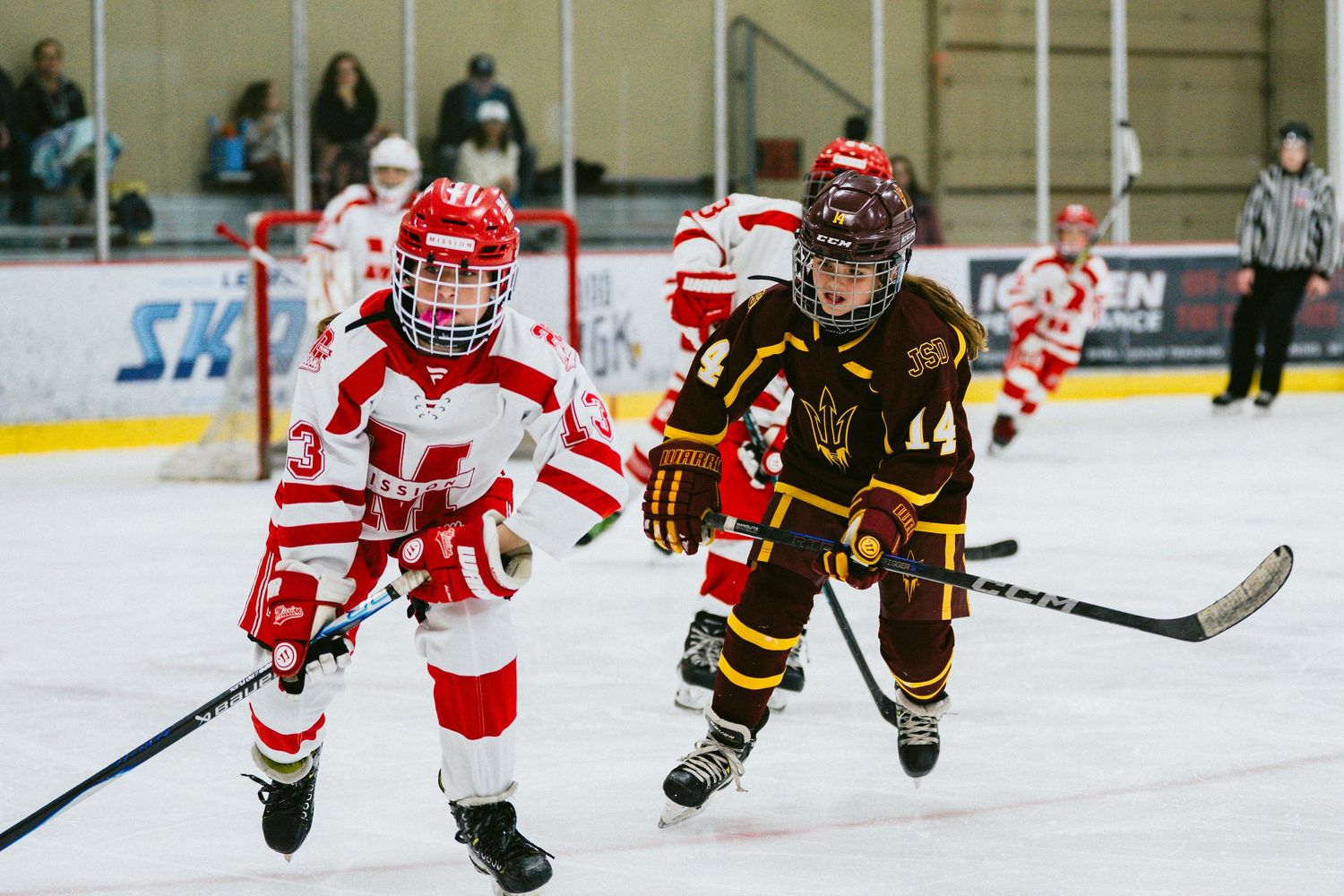 Hockey players in red and brown jerseys competing for puck during intense ice hockey match.