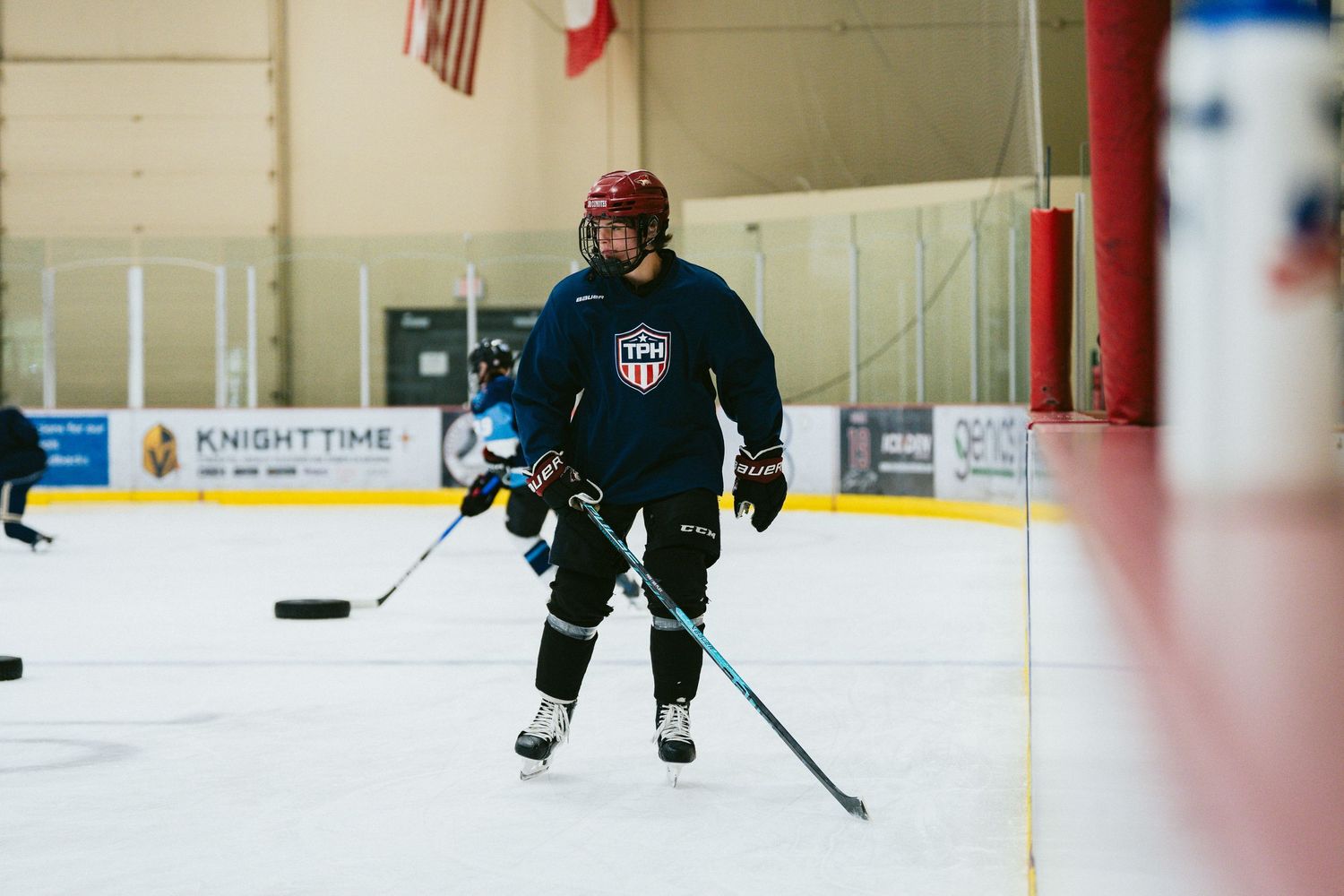 Hockey player in dark uniform skates with puck during ice rink practice session.