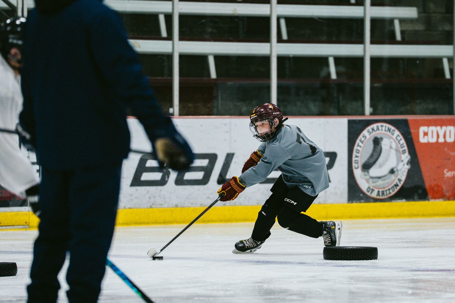 Hockey player skating with puck on indoor ice rink during practice session.