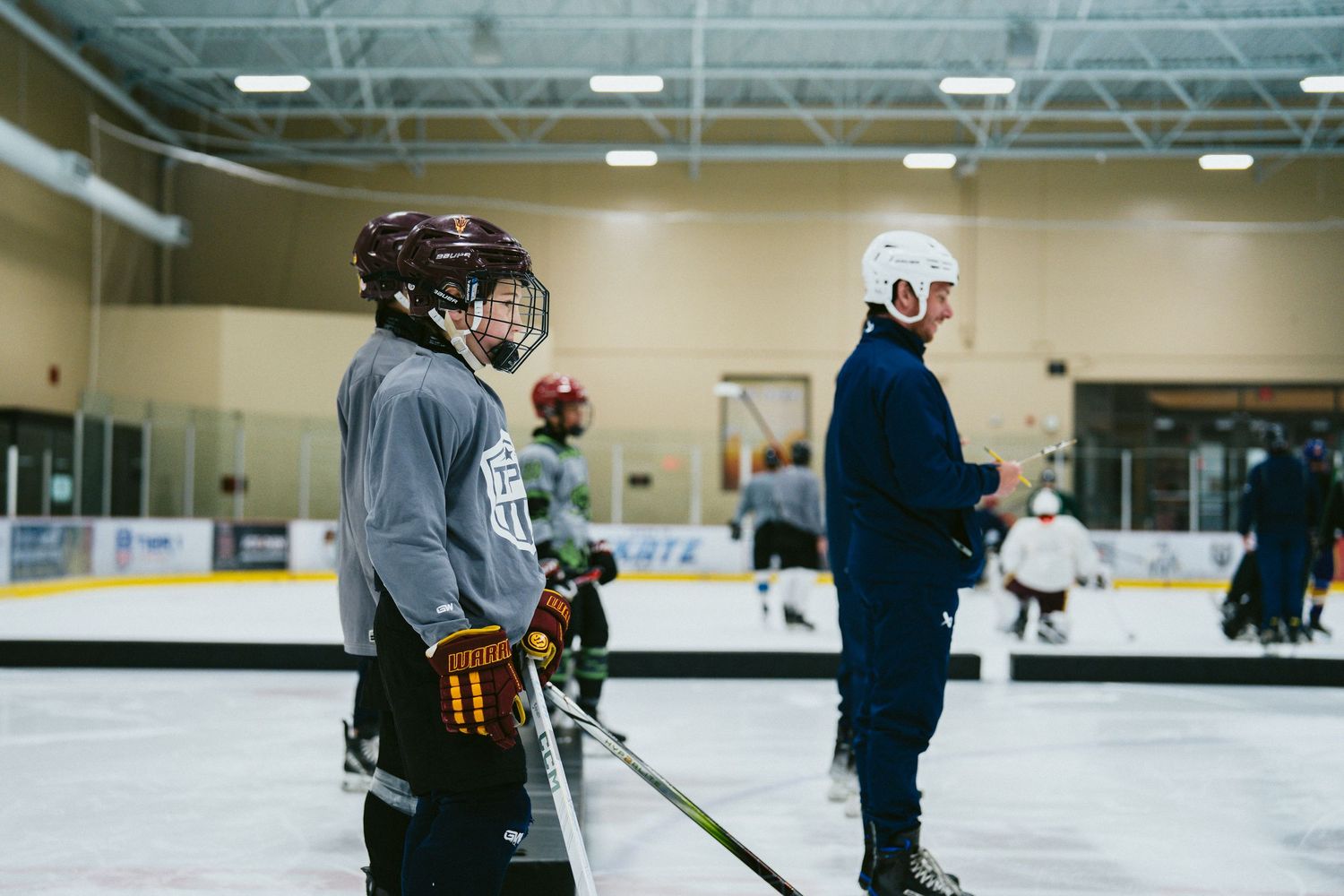 Youth hockey players stand on ice rink during practice session with coach in indoor arena.