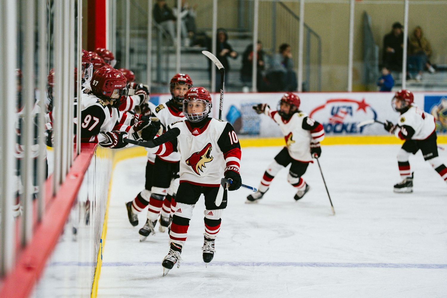 Youth hockey players in red and white uniforms skate across the ice during a game.