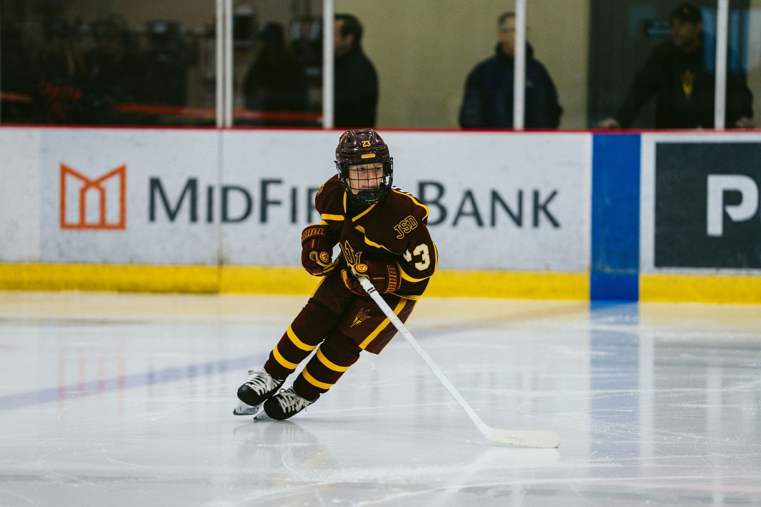 Wide shot of hockey players skating on ice with MidFirst Bank advertisement visible on arena boards.