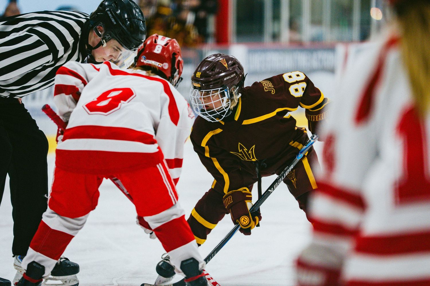 Hockey players from opposing teams face off at center ice with referee watching.