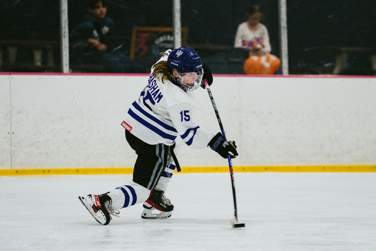 Youth hockey player in striped uniform demonstrates skating technique with puck.