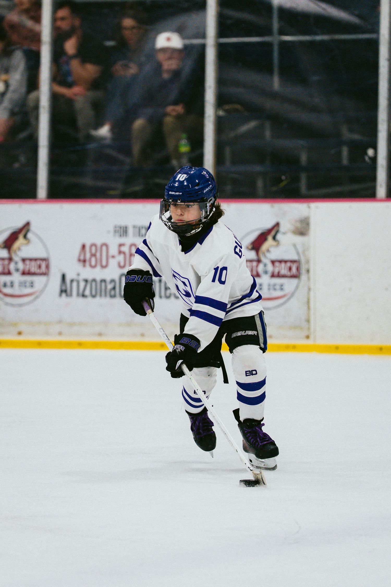 Youth hockey player in blue and white uniform skates with puck during game.