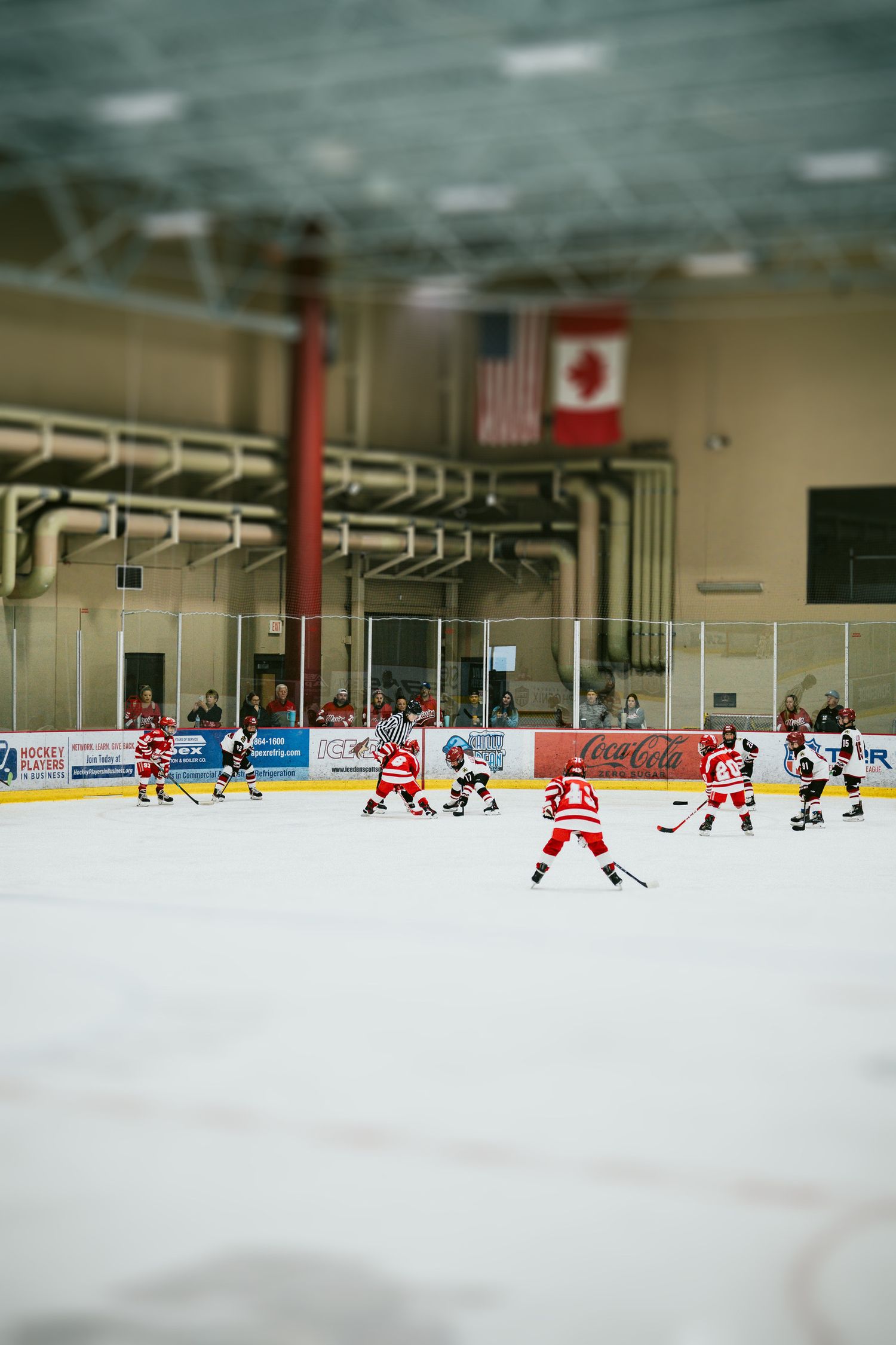 Wide angle view of youth hockey game in progress at indoor ice rink.