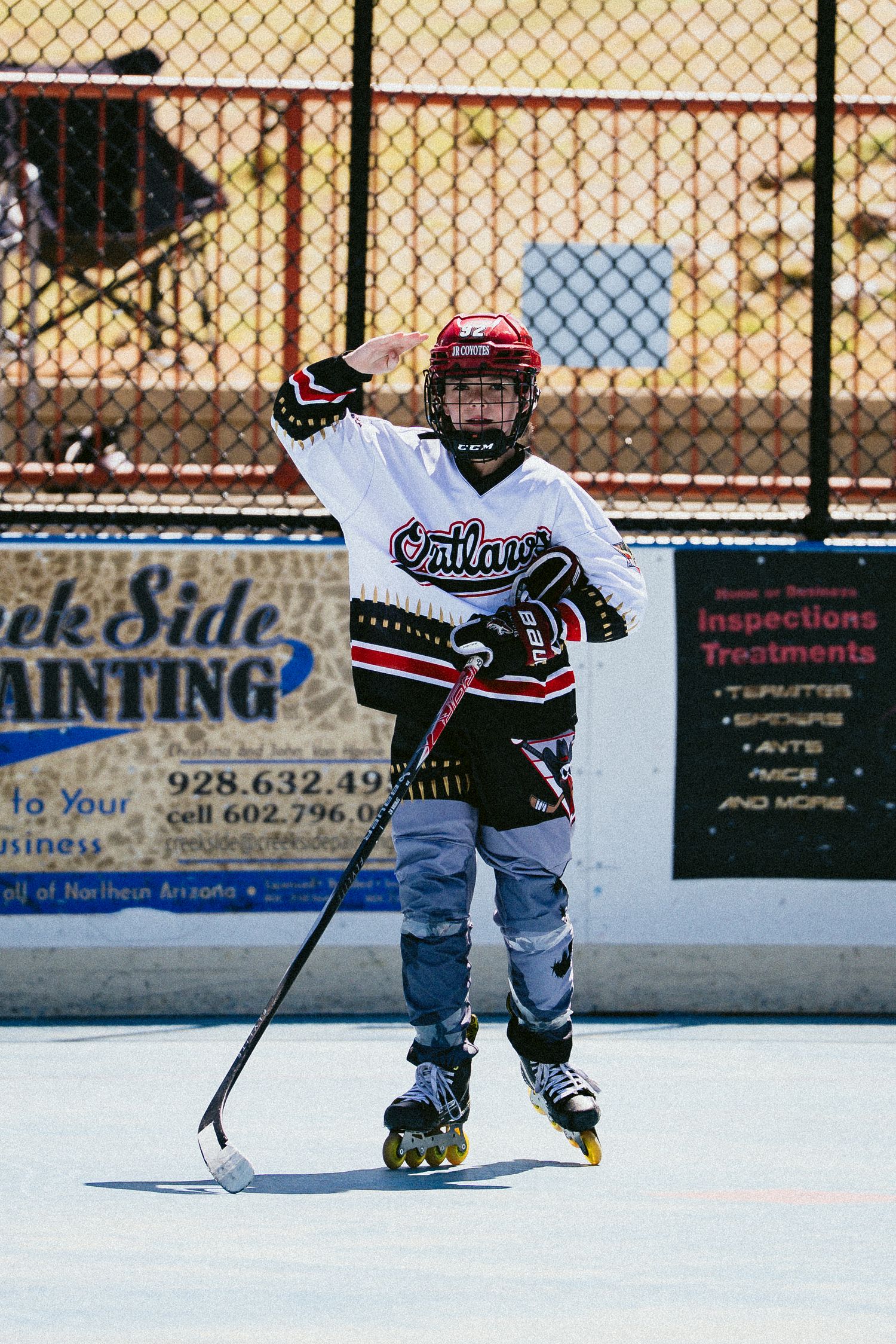 Young roller hockey player in Outlaws jersey posing with stick on outdoor rink.