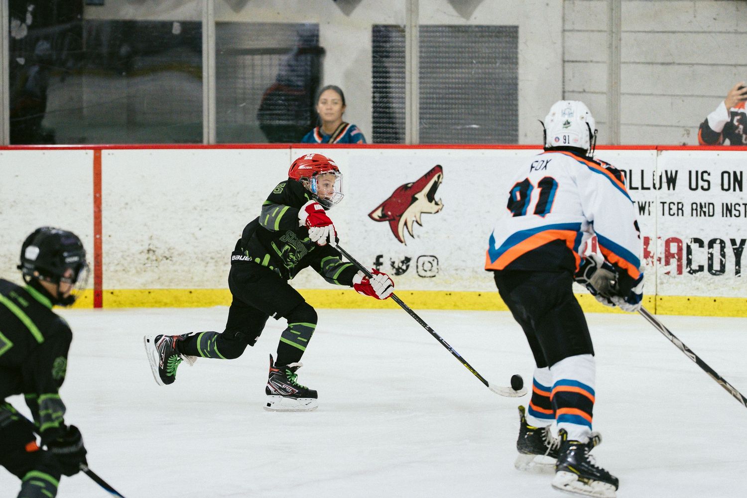 Young hockey players in green and white jerseys compete during a youth ice hockey game indoors.