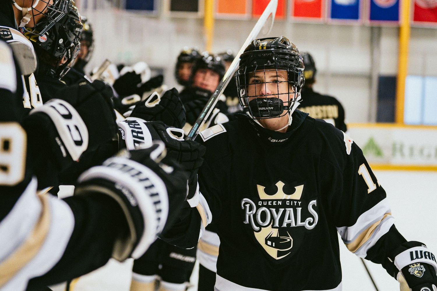 Hockey player in black Royals jersey celebrates with teammates on the ice rink during a game.