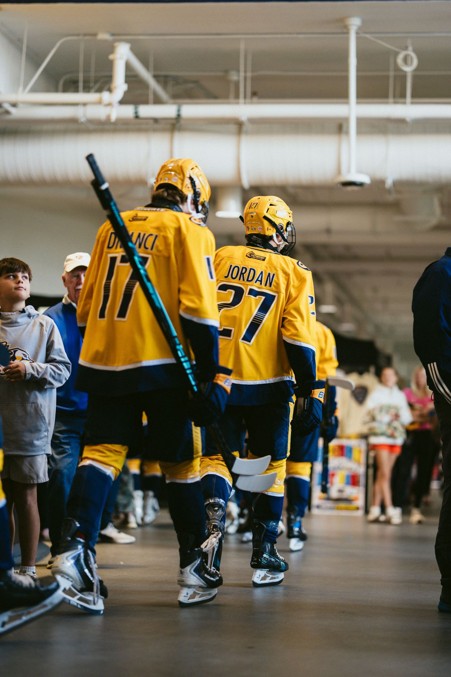 Nashville Predators players #17 and #27 Jordan in yellow jerseys walk through arena tunnel with fans watching.