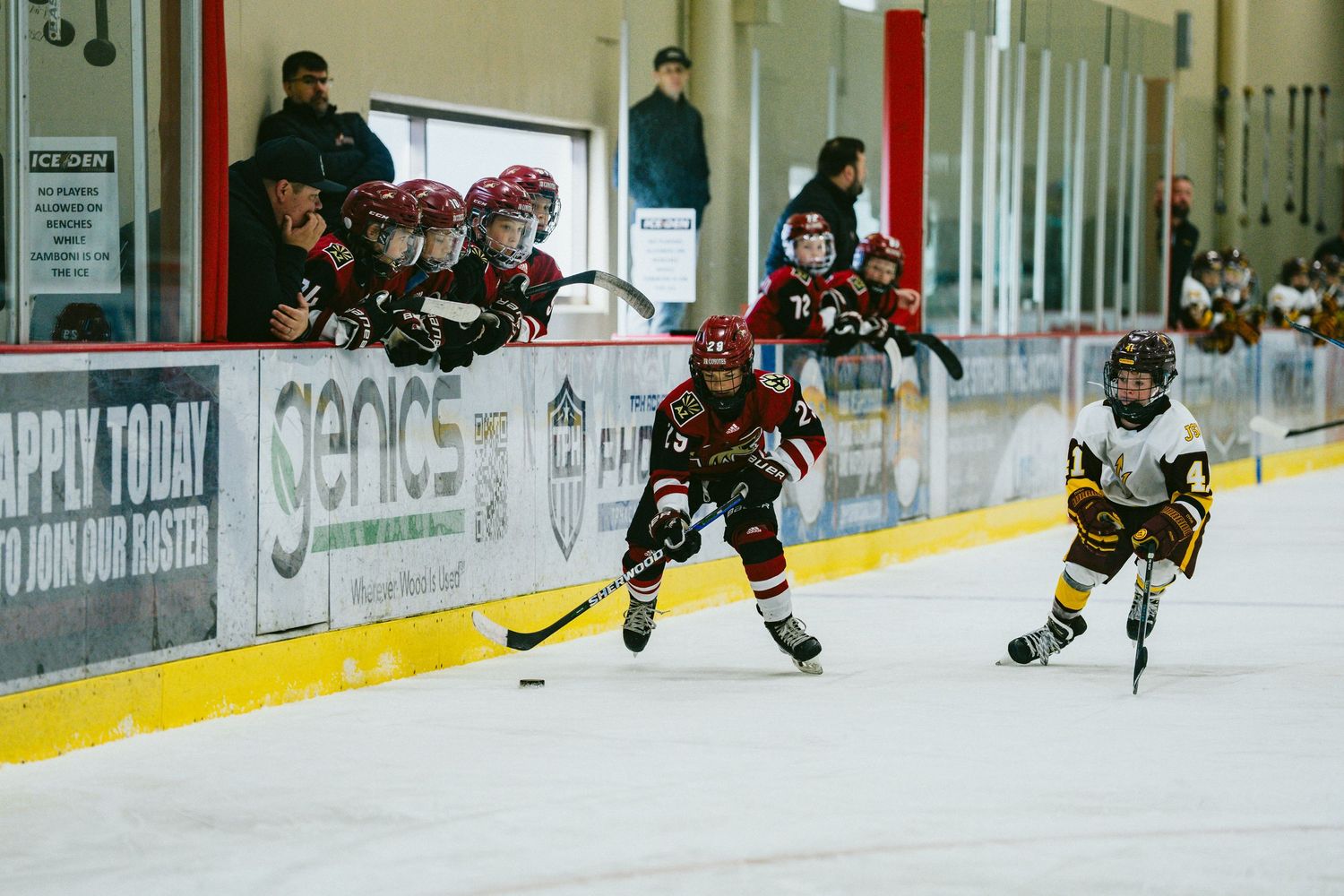 Youth hockey players compete on the ice during an intense game with players from opposing teams in action.