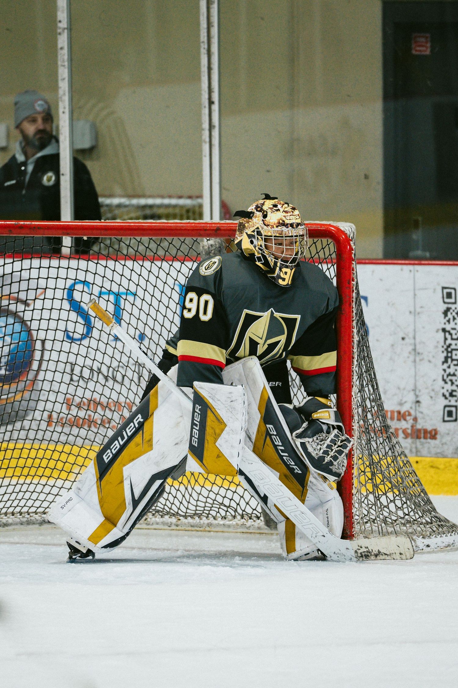 Goalie in black and gold uniform demonstrates proper positioning in front of the hockey net.