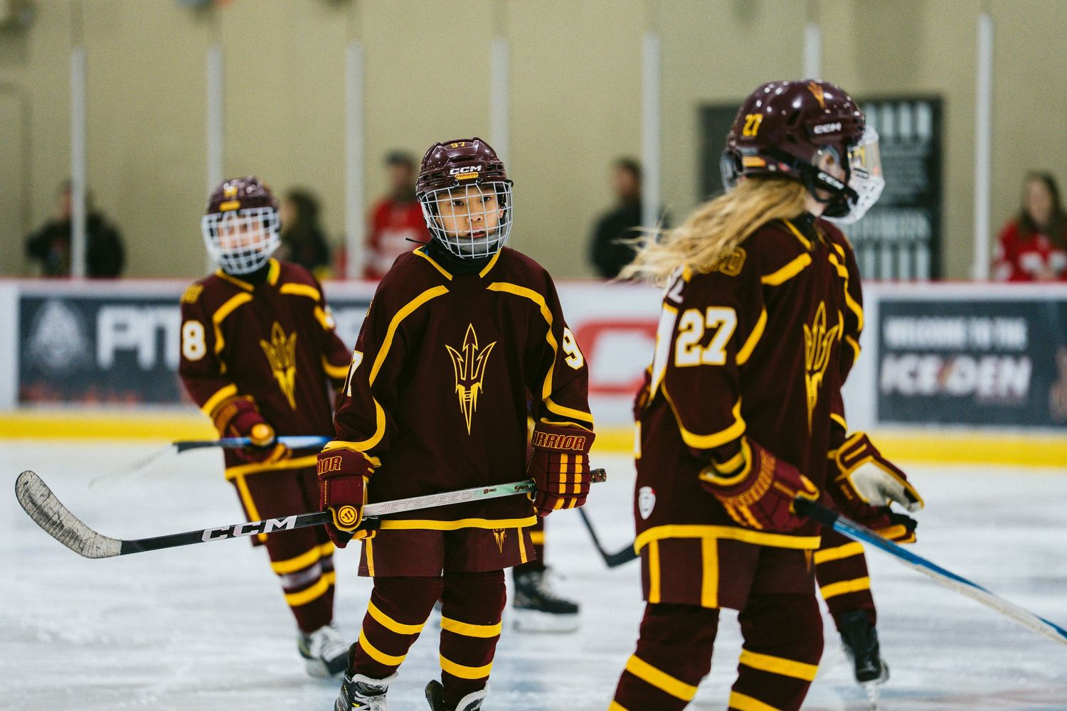 Youth hockey players in dark uniforms line up across the ice during a game.