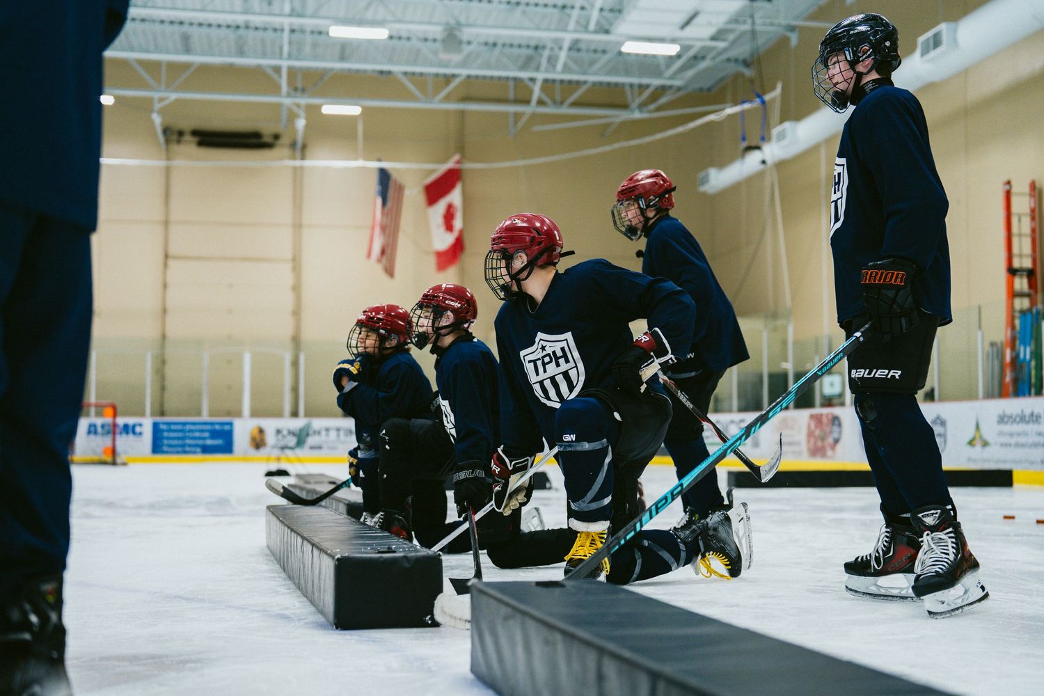 Youth hockey players in red helmets waiting on bench during ice rink training session.