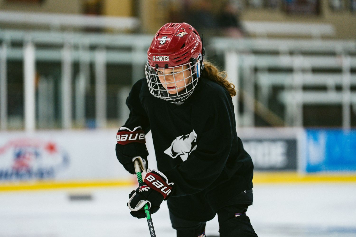 Young female hockey player in red helmet and black jersey focusing during ice hockey practice.