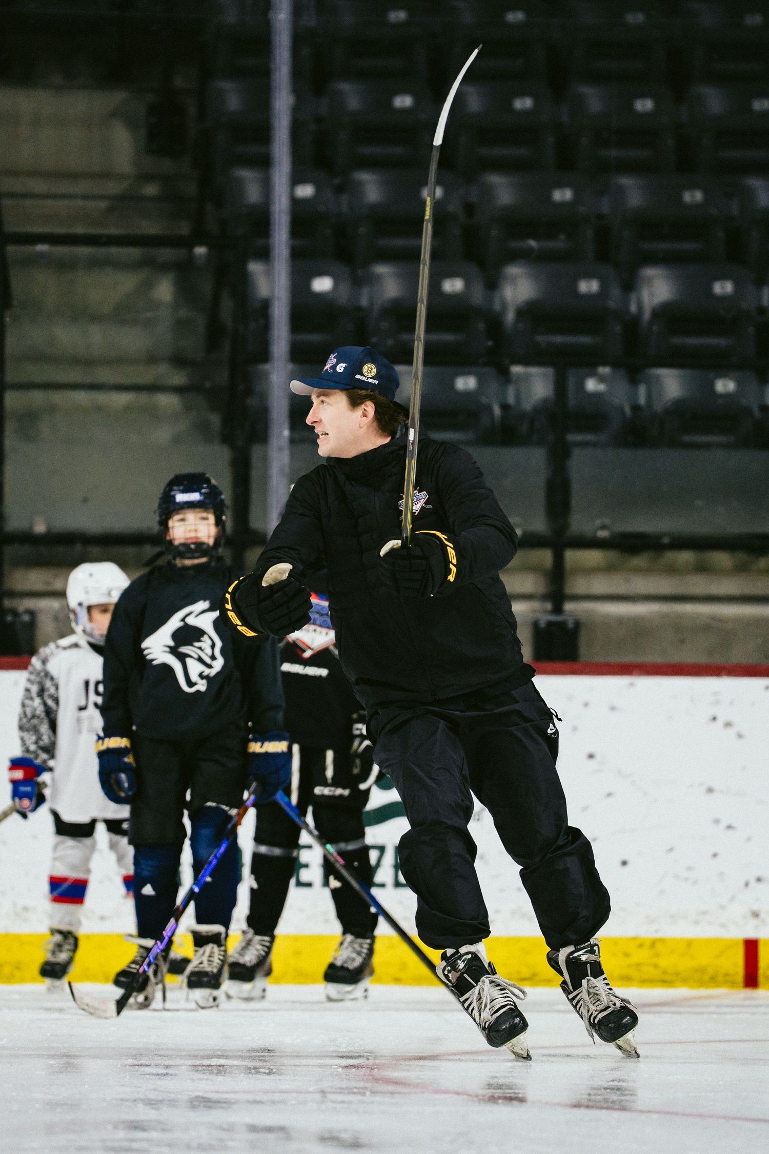 A hockey coach demonstrates a stick skill to young players during an indoor ice hockey training session.