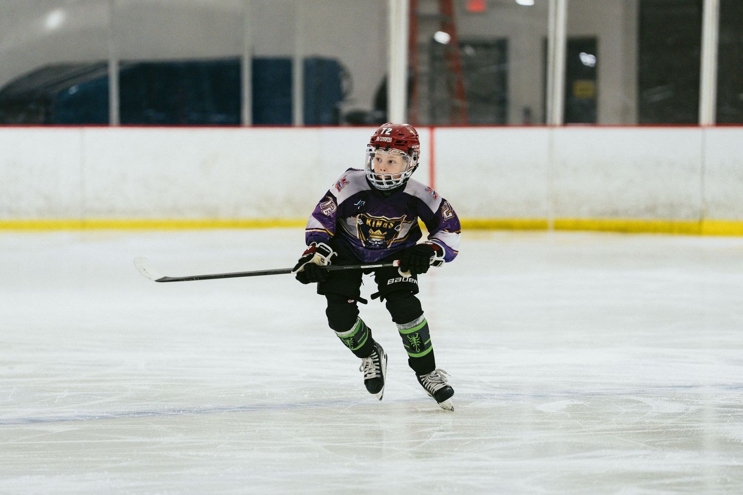 Young hockey player in purple and black uniform skating with a stick on an indoor ice rink.