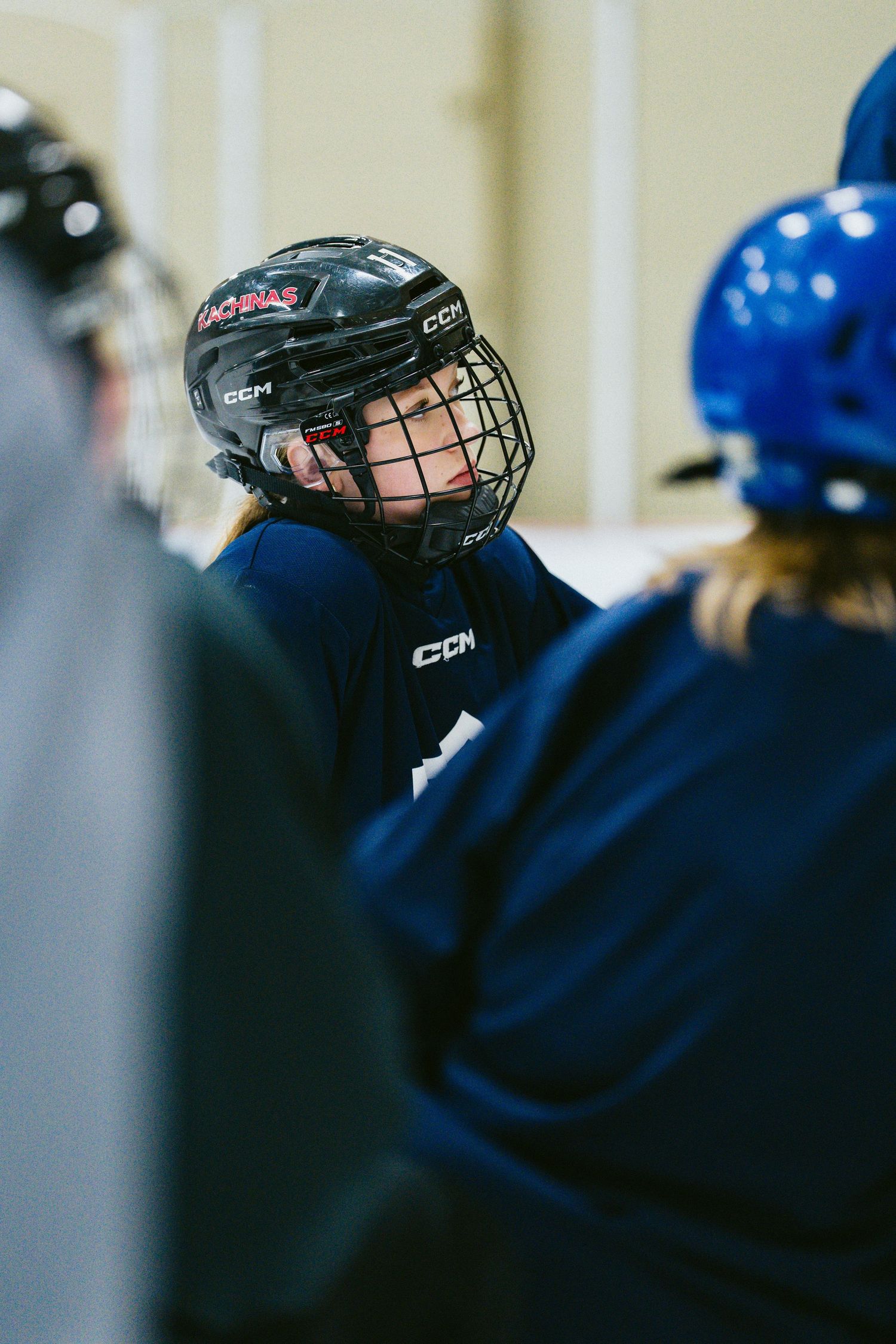 Young hockey player in CCM helmet and cage listens attentively during team huddle at indoor rink.