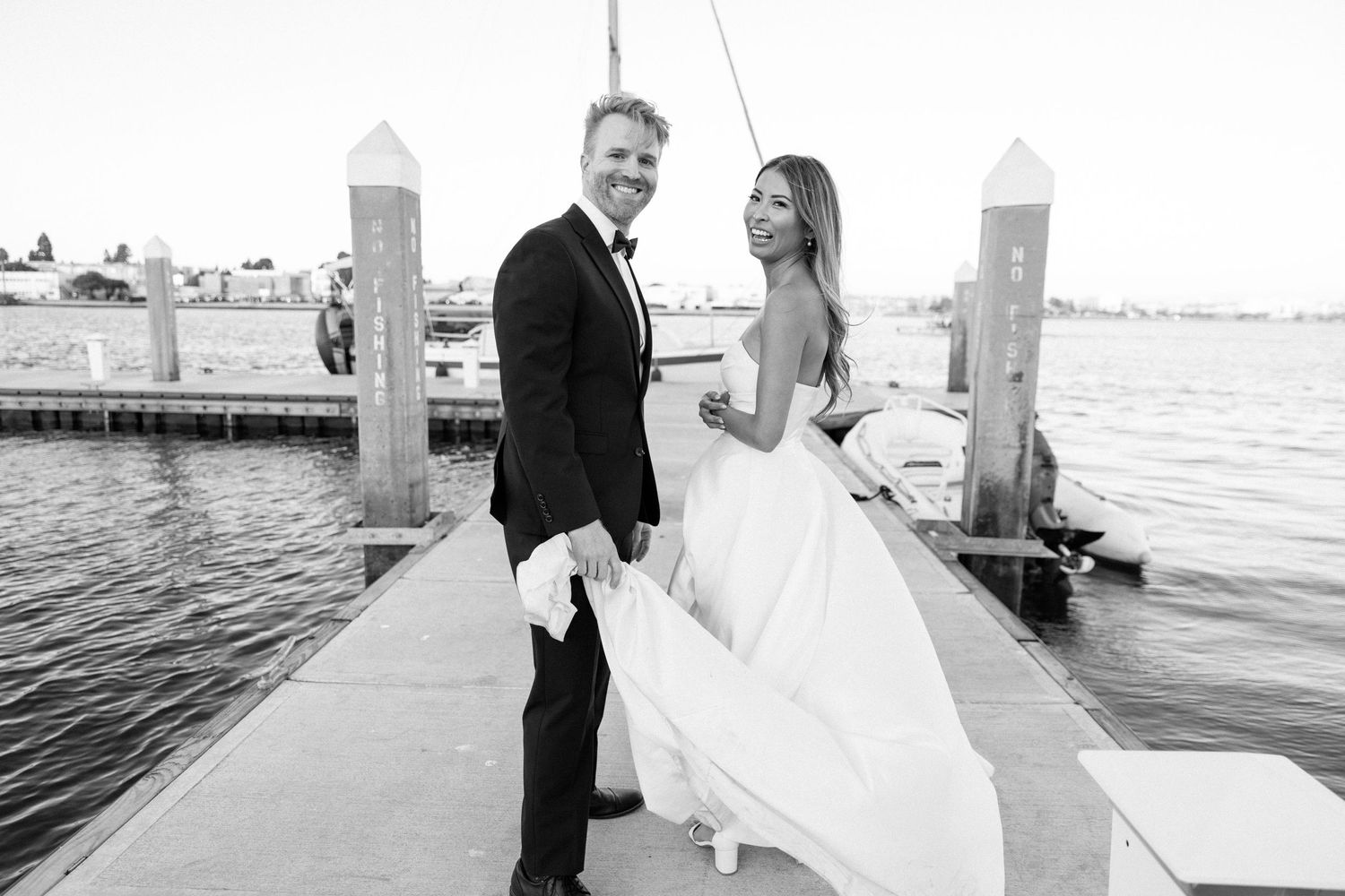 Wedding couple posing on wooden dock by waterfront.