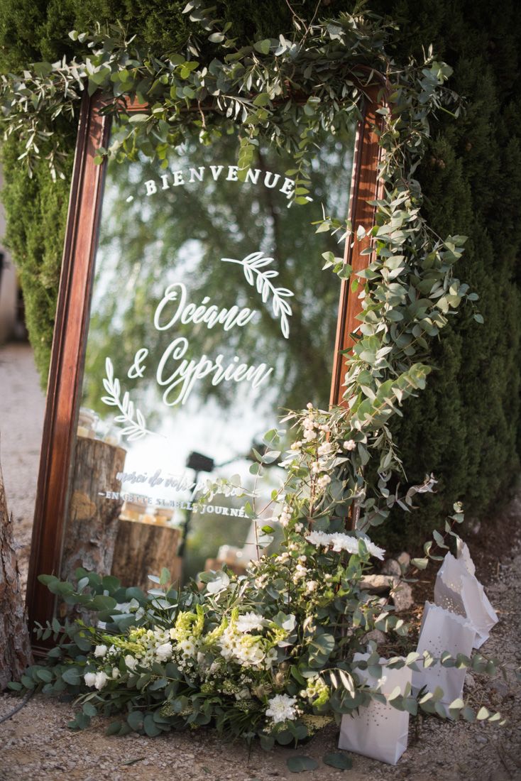 Elegant wedding welcome mirror sign reading Bienvenue Oceane and Cyprien adorned with lush greenery.