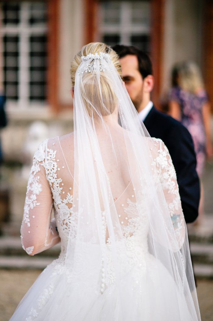 Close-up back view of bride showcasing intricate lace long-sleeve wedding gown and floral cathedral veil.