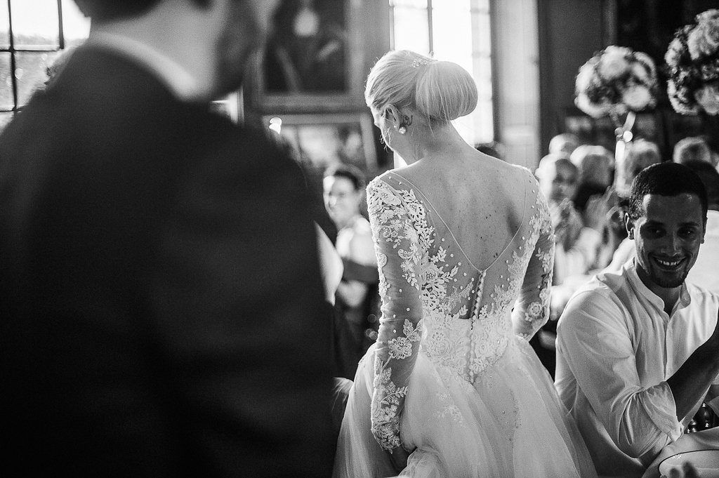 Black and white photo showcasing intricate lace back detail of bride's wedding gown at ceremony.