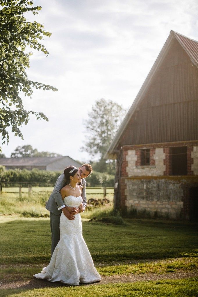 Couple shares romantic moment beside rustic stone barn in warm golden sunset light.