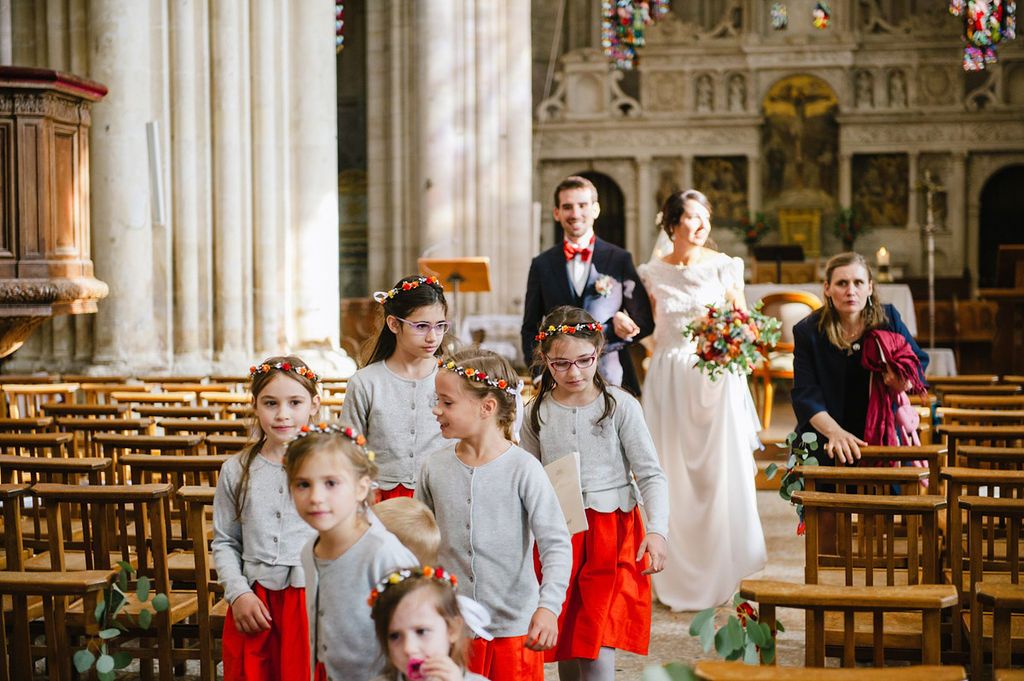 Bride and groom pose with flower girls in matching red and white outfits inside a church.