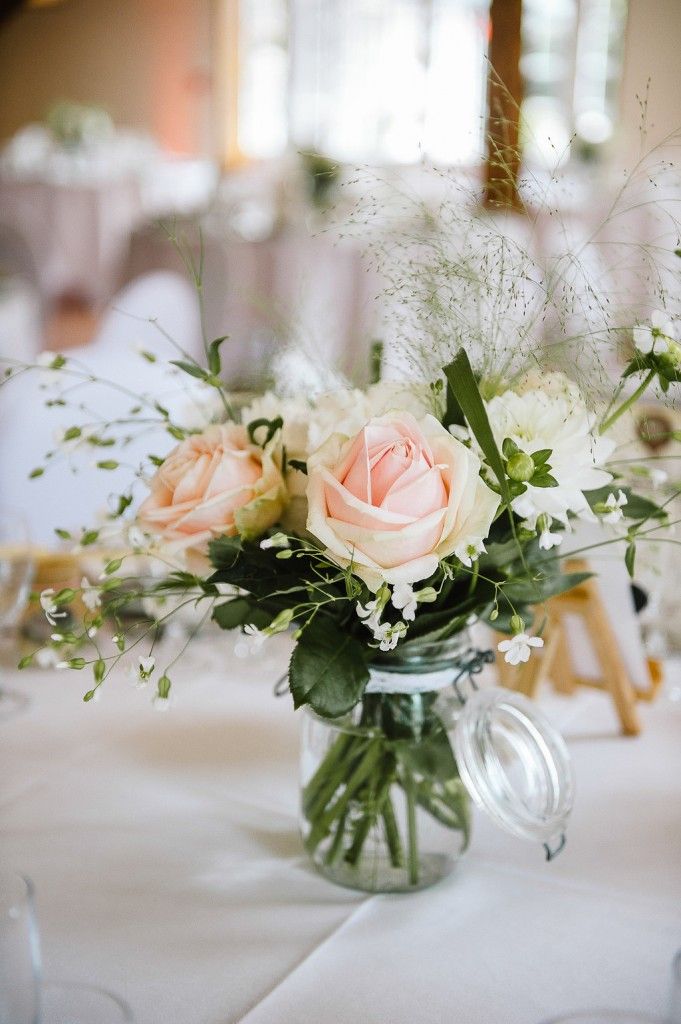 Romantic wedding centerpiece with blush pink roses and white flowers in a glass mason jar.