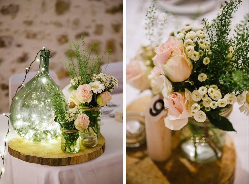 Elegant wedding table centerpieces featuring pink roses, white flowers, and a glass bottle with fairy lights.