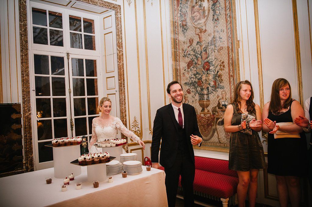Bride and groom smile beside dessert table display at elegant chateau wedding reception.