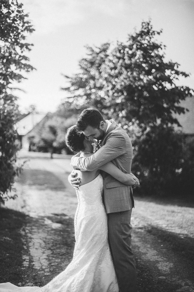 Bride and groom share passionate embrace on country path in black and white photo.