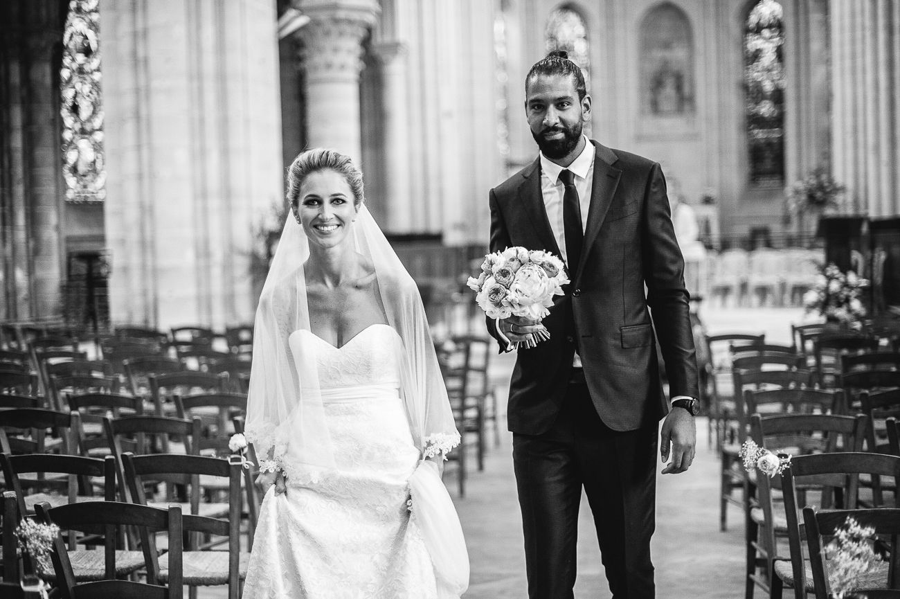 Black and white photo of a bride and groom walking down the aisle of a church after their wedding ceremony.