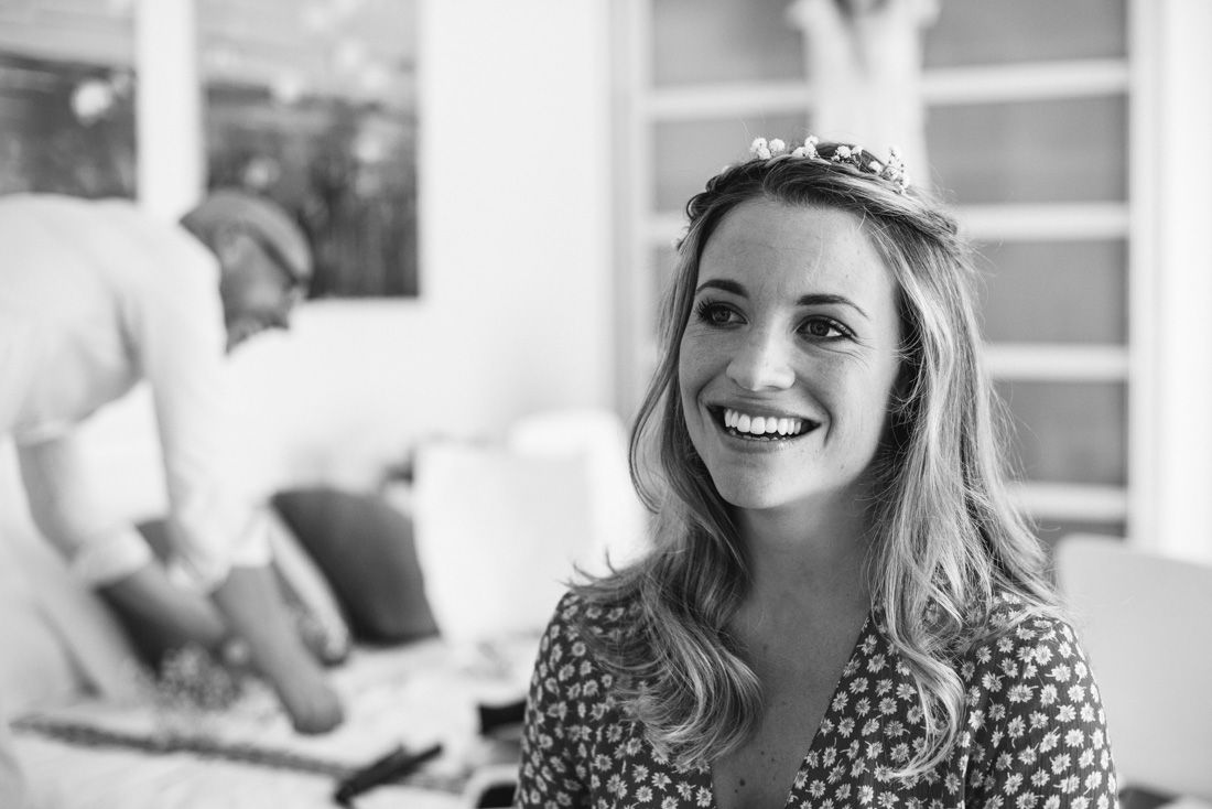 Smiling bride wearing a floral crown tiara with long wavy hair in a black and white wedding preparation photo.