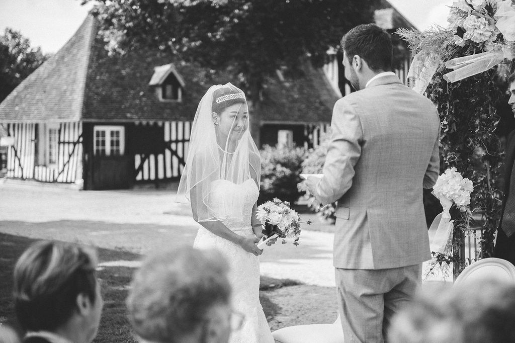 Bride and groom exchange vows outdoors at a rustic wedding ceremony with a charming timber-framed barn in the background.