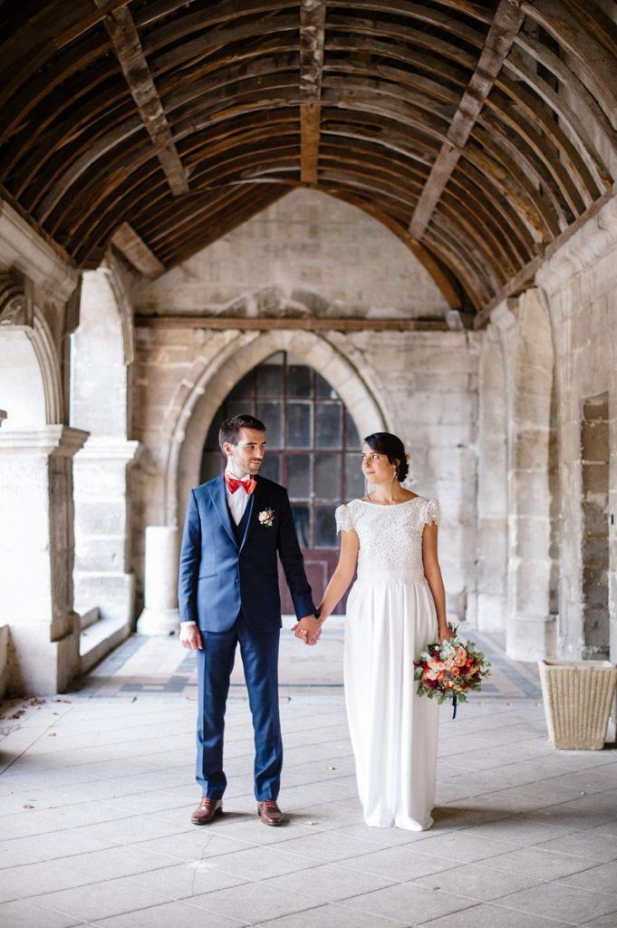 Bride and groom holding hands in a historic stone archway corridor on their wedding day.