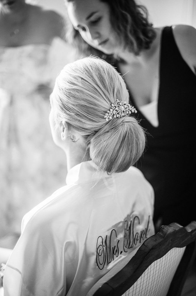 Black and white photo of bride with elegant updo and crystal hair accessory being styled.