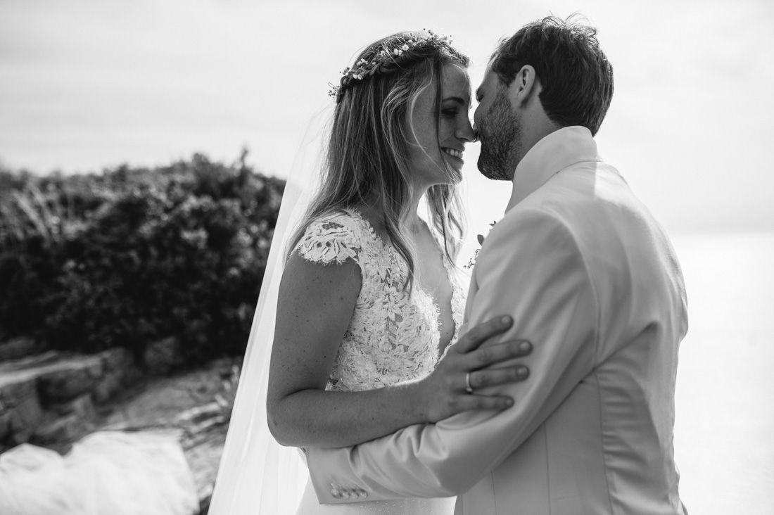 Black and white beach wedding photo of bride and groom sharing a romantic moment, bride in lace dress with veil.