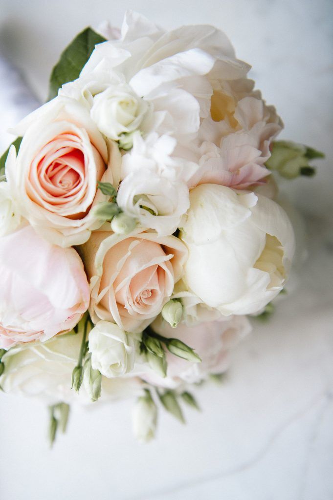 Close-up of romantic bridal bouquet featuring blush roses, white peonies, and small white blooms.